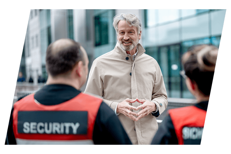 Peter Karst im Gespräch mit zwei Sicherheitskräften vor einem Bürogebäude
